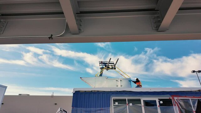 Construction worker hoisting air unit on rooftop