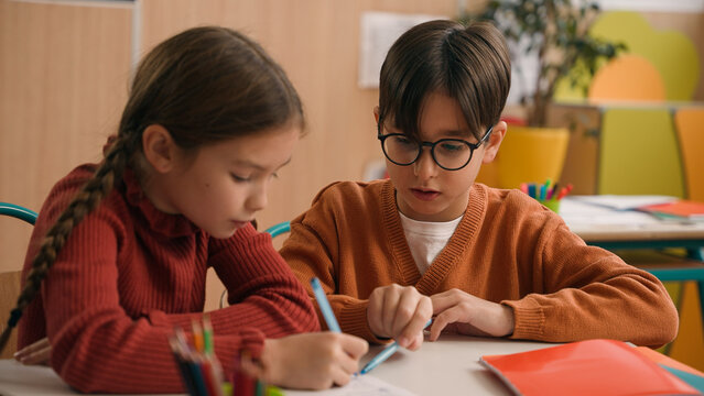 Two Caucasian pupils classmates in school lesson class together write little boy help girl kid child with test homework helping explain task studying children education learning learn teamwork friends