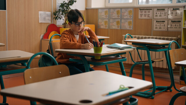 Alone little boy in empty school class room sitting at desk table writing homework clever Caucasian primary school child kid son pupil learning task write notes lesson studying elementary education
