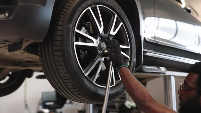 Mechanic using tool to work on car wheel in auto repair shop. Man wears gloves and glasses while focused on task. Bright and spacious workshop in background.