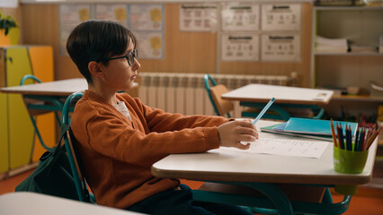 School class lesson clever concentrated Caucasian boy son child schoolboy kid studying learning in classroom write test exam task study learn primary education write knowledge classwork at table desk