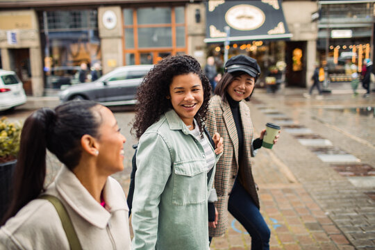 Three diverse female friends walking together on city street
