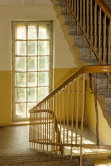 Obraz premium Staircase and window illuminated by the sun in the old entrance of an old house.