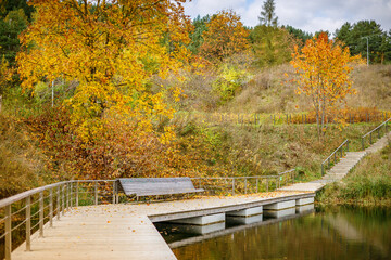 A serene park in Vilnius during autumn, featuring a wooden pier with a bench overlooking a...