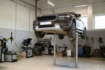 Car elevated on hydraulic lift in professional auto repair shop with tools and equipment. Modern workshop environment for vehicle maintenance and inspection.