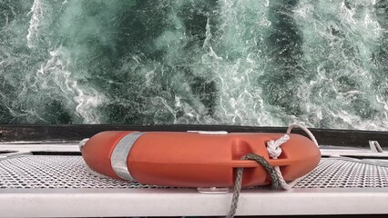 A red life preserver sits on a railing next to the water