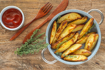 Pan of oven baked potato chips and tomato sauce over wooden background.

