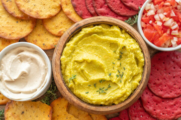 Creamy avocado dip for tasty and healthy snack on the background of salsa sauce, vegetable cookies, tahini pasta and fresh thyme. Top view.