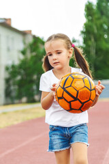 Cute child girl playing on sports ground with soccer ball outdoors