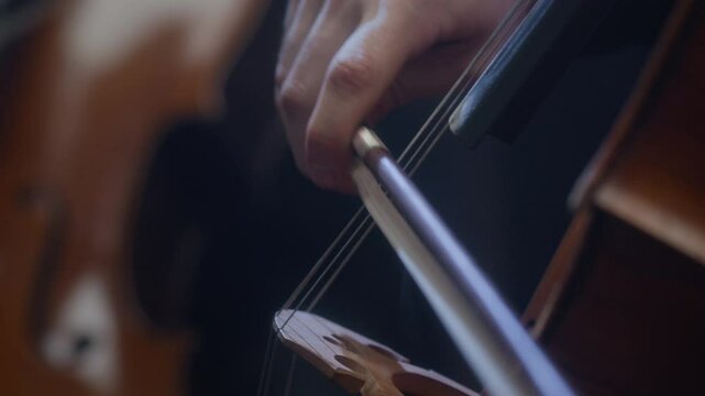 Closeup of unrecognizable male hand of musician playing cello with bow during orchestra concert