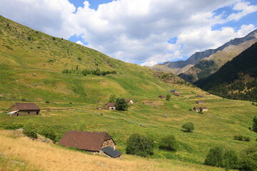 Historiacal Viados village in Spanish Pyrenees. Old, stone shepherd's huts among green meadows, with huge, rocky walls of Posets Massif fulfilling upper parts of the image next to Benasque