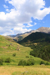 Obraz premium Historiacal Viados village in Spanish Pyrenees. Old, stone shepherd's huts among green meadows, with huge, rocky walls of Posets Massif fulfilling upper parts of the image next to Benasque