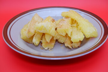 Fried cassava served on a plate. Fried cassava dish isolated on a red background.