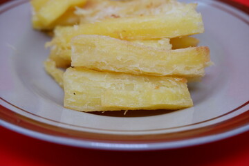 Fried cassava served on a plate. Fried cassava dish isolated on a red background.