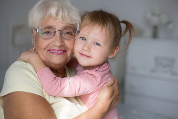 Happy loving granddaughter child hugging excited blonde grandma from behind at home. Grandmother and kid girl enjoying funny leisure on family meeting, having fun, laughing