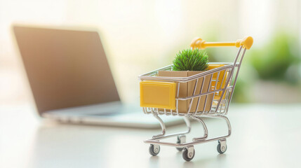 A small shopping cart with a plant sits beside a laptop, symbolizing sustainable online shopping and eco-friendly choices.