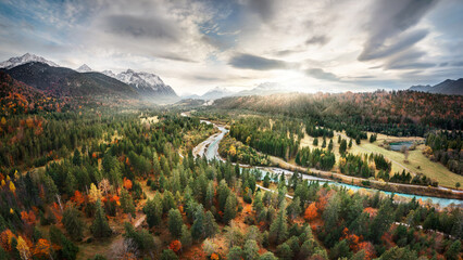 Aerial autumn scenery with colorful forest, dramatic sky and a river leading toward the sun and the...