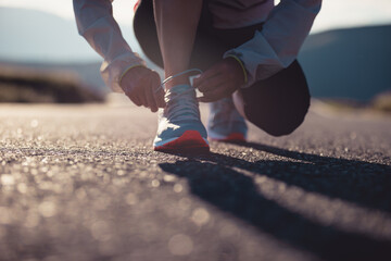 Woman runner tying shoelace on sunset mountain road