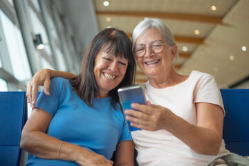 Smiling senior couple of female friends sitting in airport departure area waiting for boarding...