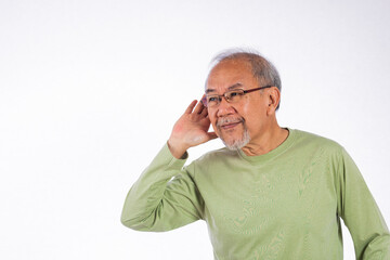 Portrait Asian old man with glasses and a beard listening to sound something, possibly engaged in conversation or trying to understand a message, hand on ear hearing a rumor isolated white background