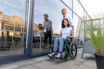 Man carrying a wheelchair of his wife and looking at her with love