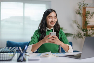 Young asian businesswoman is smiling while using a smartphone at her desk in her home office