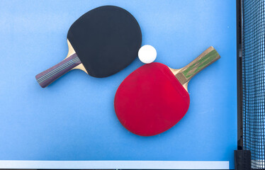 Red and black rackets for table tennis with white ball on blue background. Ping pong sports equipment in minimal style. Flat lay, top view, copy space