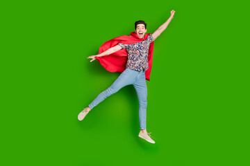 Full size photo of overjoyed guy dressed print shirt red cloak fly to empty space raising fist up isolated on green color background