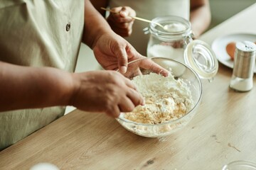 Close up on hands of senior Black woman stirring baking powder and eggs in glass bowl for making...
