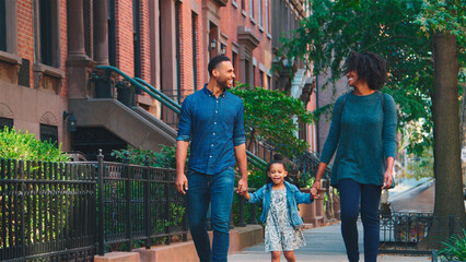 Family Shot With Parents Holding Hands With Daughter As They Walk Along Street In New York City 