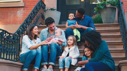 Two Families With Young Children Sitting Steps Outside Home Together On Urban Street In New York City