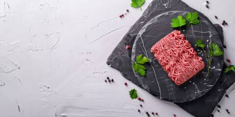 Top view of fresh ground beef on a round slate stone. Parsley and pepper on a white background.