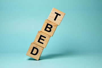 Wooden alphabet blocks piled up to form the word DEBT, leaning, about to fall. Concept on unsustainable debt, collapse of financial system, economy due to high borrowings, unpaid mounting loans.