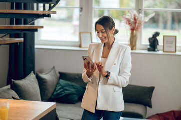 Woman in white jacket standing in the middle of the room and looking contented