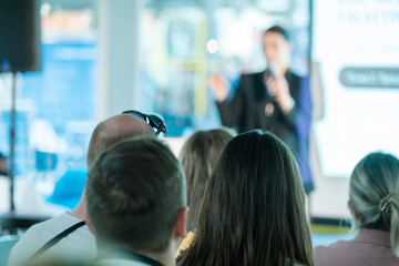 Audience attentively listening to a speaker presenting at a business event. Blurred backdrop with...