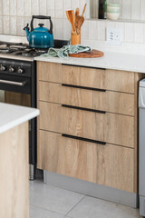 Wood look kitchen cabinet drawers with a white stone counter top, hidden black handles, black free standing cooker and styled kitchen elements