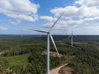 Aerial front view of a wind turbine in the wind. Sweden, summer, forest and meadows. Sunshine and patchy clouds.