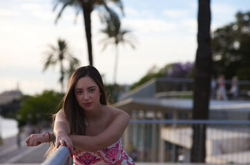 Young, pretty, blonde Spanish woman rests her outstretched arm on the iron railing looking at the...