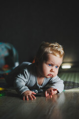 Fototapeta premium Cute blond toddler boy playing with baby toys at home sitting on carpet in living room. Smiling cute little child using colorful toys, chewing teether