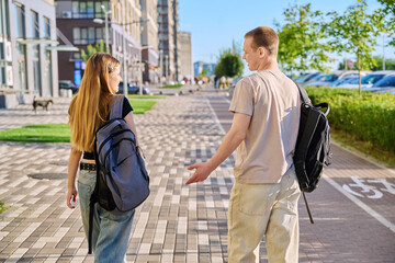 Guy and girl, college students walking together along street of city, back view