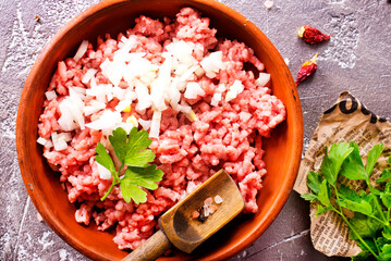 Homemade minced meat with ingredients for making in a bowl over dark slate, stone or concrete background.