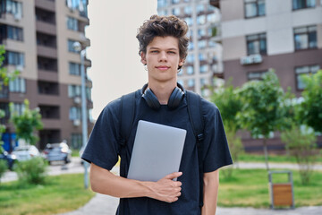 Portrait young male college student with backpack laptop, outdoor urban background