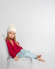 Portrait of beautiful cute little toddler girl. Child with funny face in burgundy color sweatshirt and white hat. Pretty smile kid in studio on light background. Vertical photo