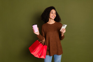 Portrait of pretty young woman phone coffee bags look empty space wear sweater isolated on khaki...