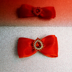 on a gray shiny background lies a bright red bow with large stones in the middle with a reflection on a red background. hair accessories, for dog hair. top view. Christmas