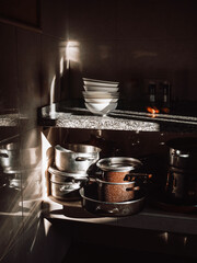 A dimly lit kitchen corner with dramatic sunlight streaming in, illuminating stacked bowls, pots and pans.