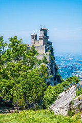 Fototapeta premium A view past trees towards the first tower in the fortified section of San Marino, Italy in summertime