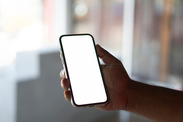 Young man Holding Smartphone with Blank White Screen in Modern Indoor Setting, Perfect for Mockups and Digital Content.