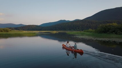 Two people paddling a canoe in tandem along a fantastic lake with mountain reflection on the water, aerial shot. Nature enjoyment moment concept. - Powered by Adobe