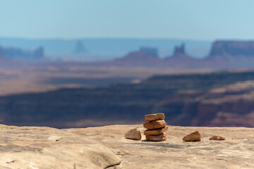 Rock stack cairn on desert cliff with Monument Valley in distant background goosenecks